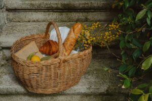 A rustic basket with bread, croissants, and flowers on stone steps.