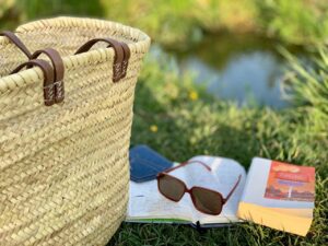A relaxing outdoor setting featuring a woven bag, sunglasses, and an open book on grass.